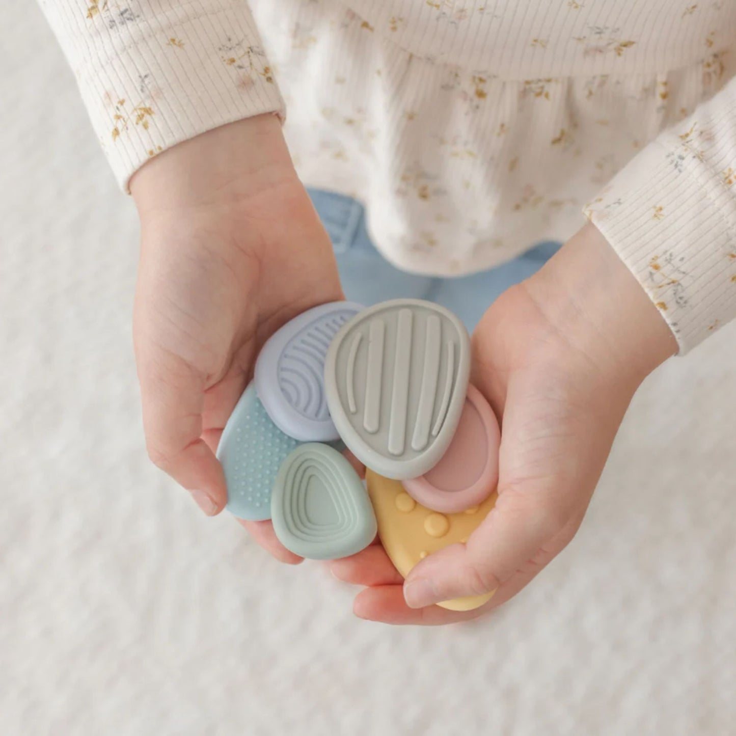 Child's hands holding four small, pastel-coloured silicone worry stones.