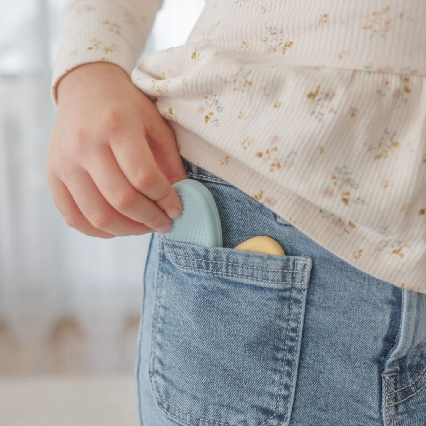 Child wearing a floral shirt and blue jeans with silicone worry stones in their pocket against a blurred background