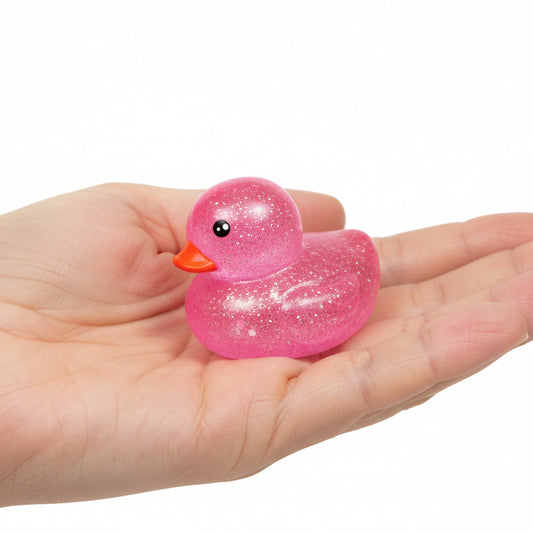 Pink glittery squishy duck held in a hand on a white background