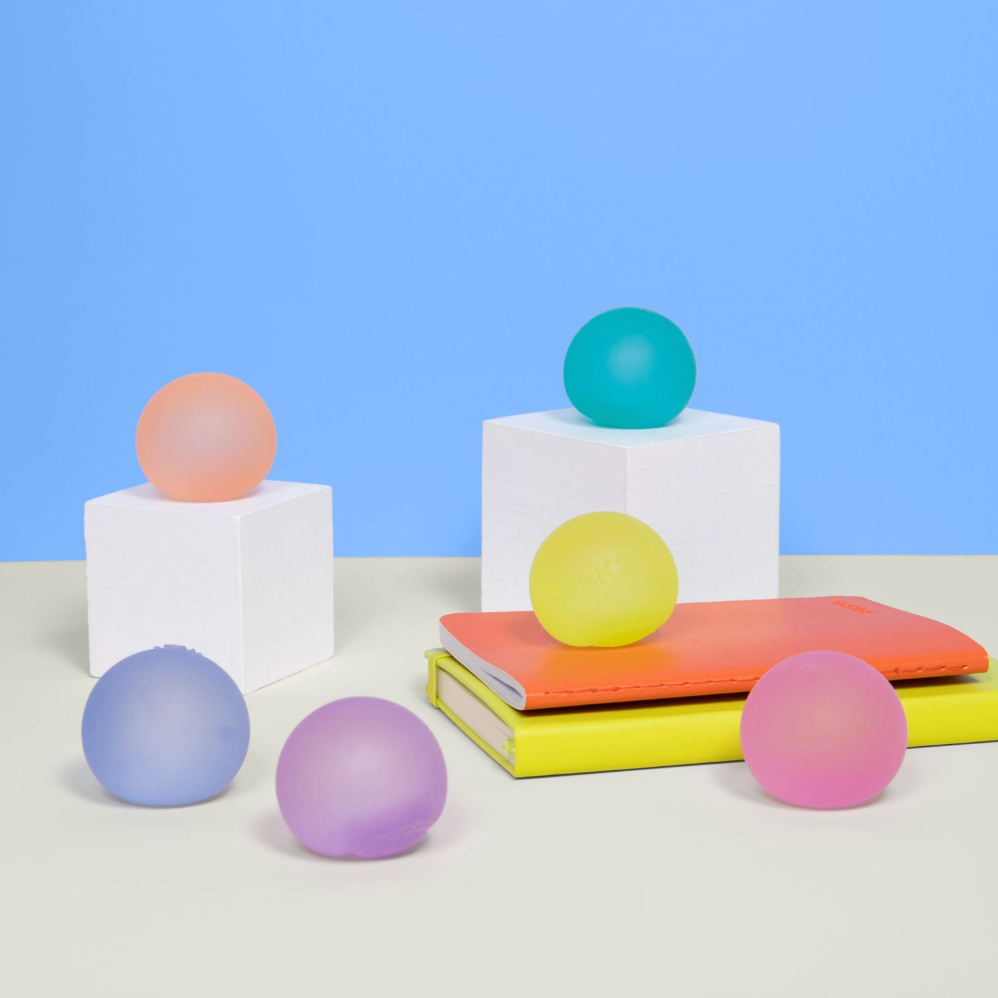 Colourful Speks mini memory gel stress balls on geometric shapes against a blue background