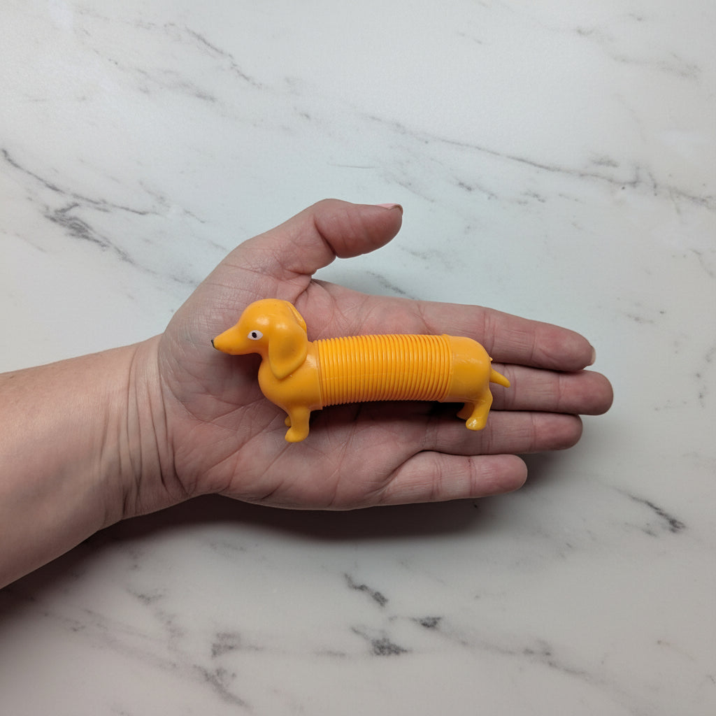 Hand holding a yellow dog-shaped toy on a marble surface