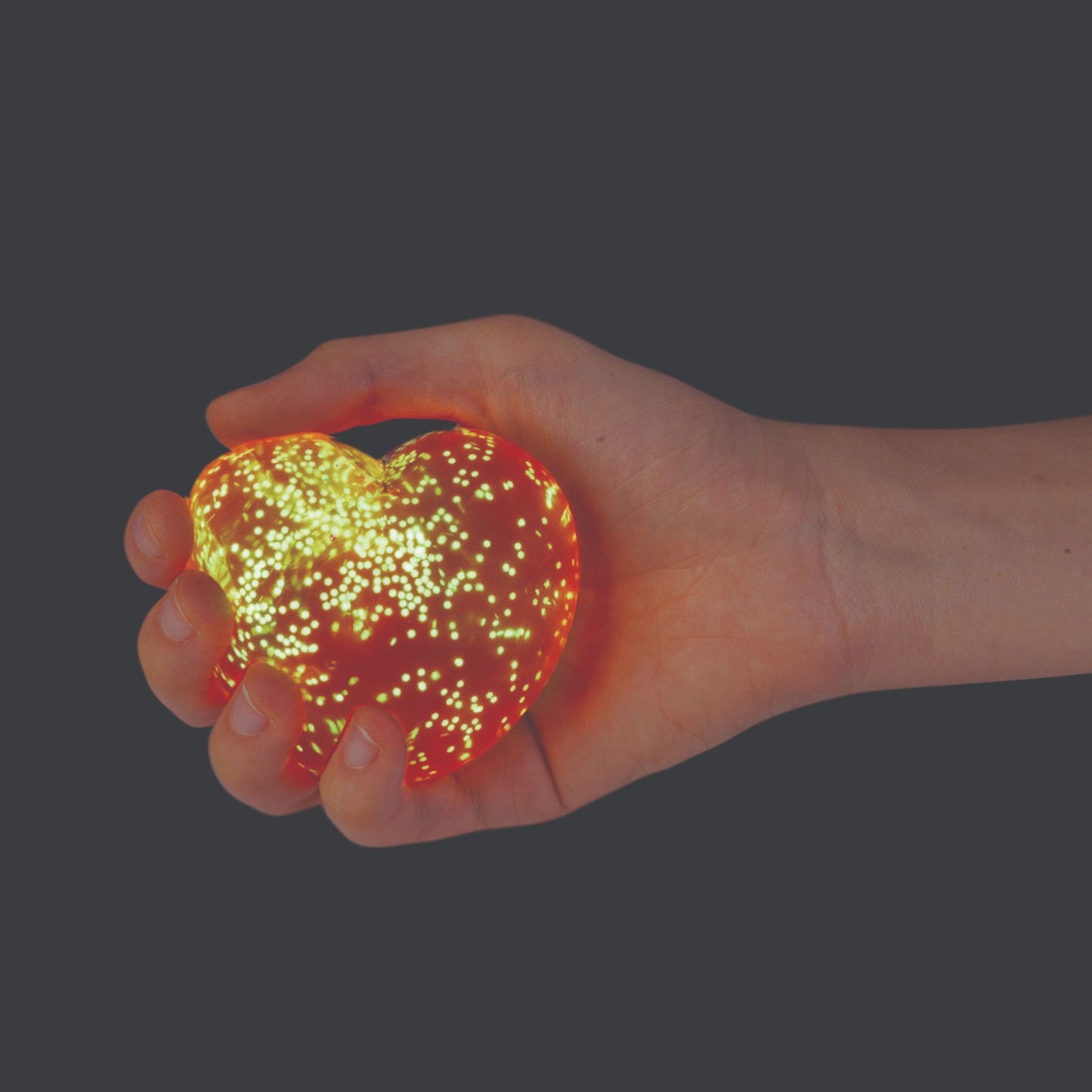 Hand holding a glowing Smooshos Super Squeeze Glow in the Dark Heart Stress Ball Squishy