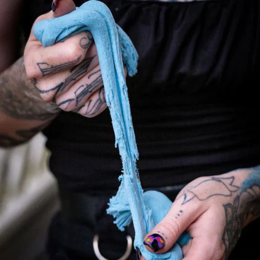 Person with tattoos holding a blue stretchy sand by Kaiko with a blurred background