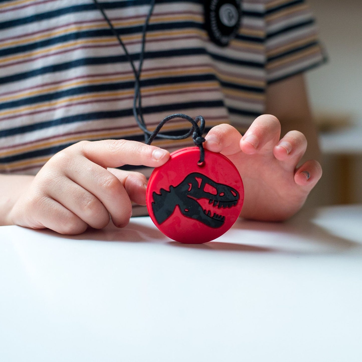 Child's hands holding Jellystone Designs Chew Necklace Dino in Red & Black