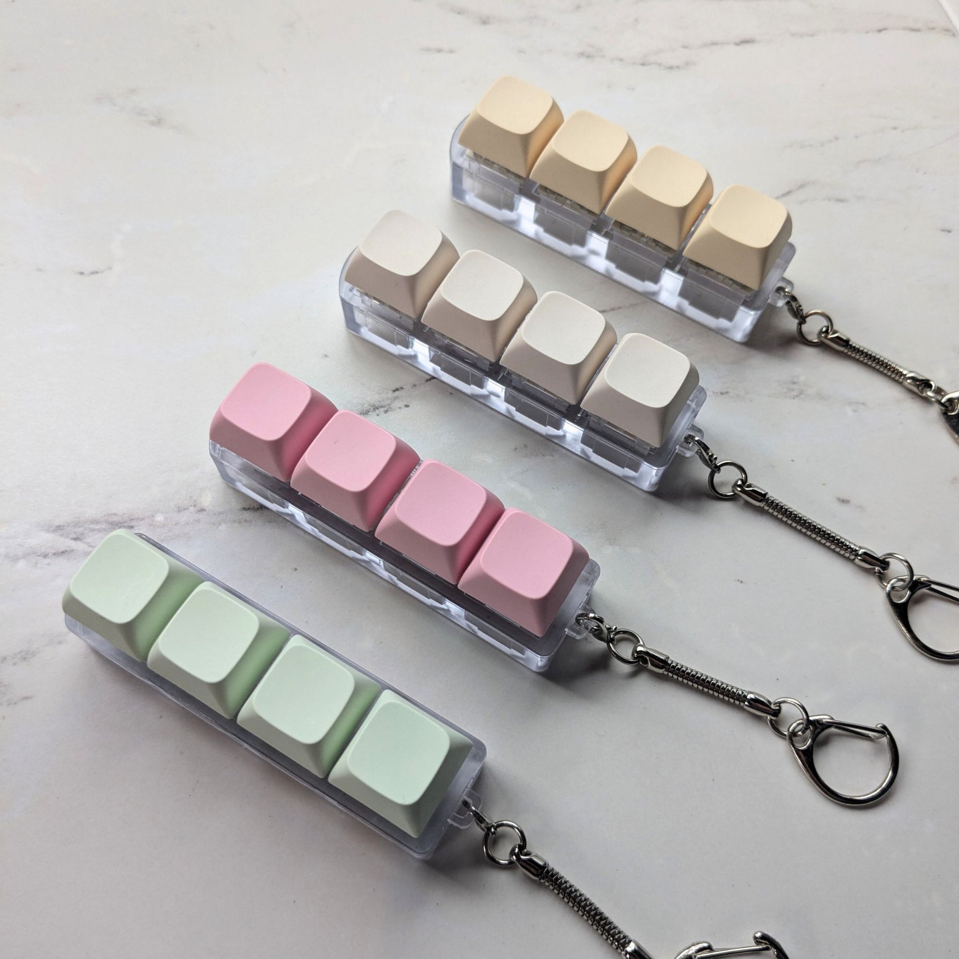 Keyboard clicky fidget keychains in green, pink, cream and beige on a light background