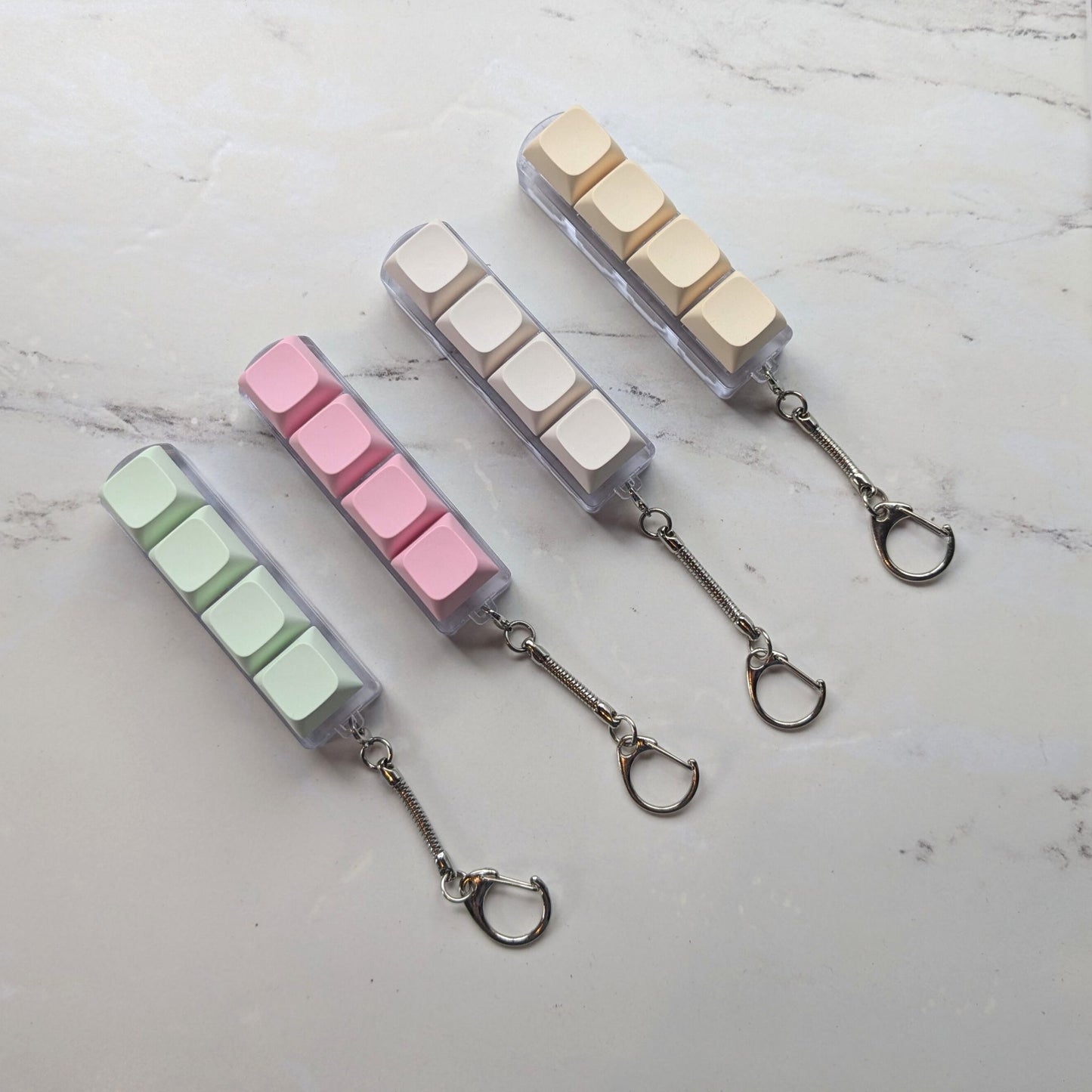 Keyboard fidget clicker keychains in green, pink, cream and beige on a light background