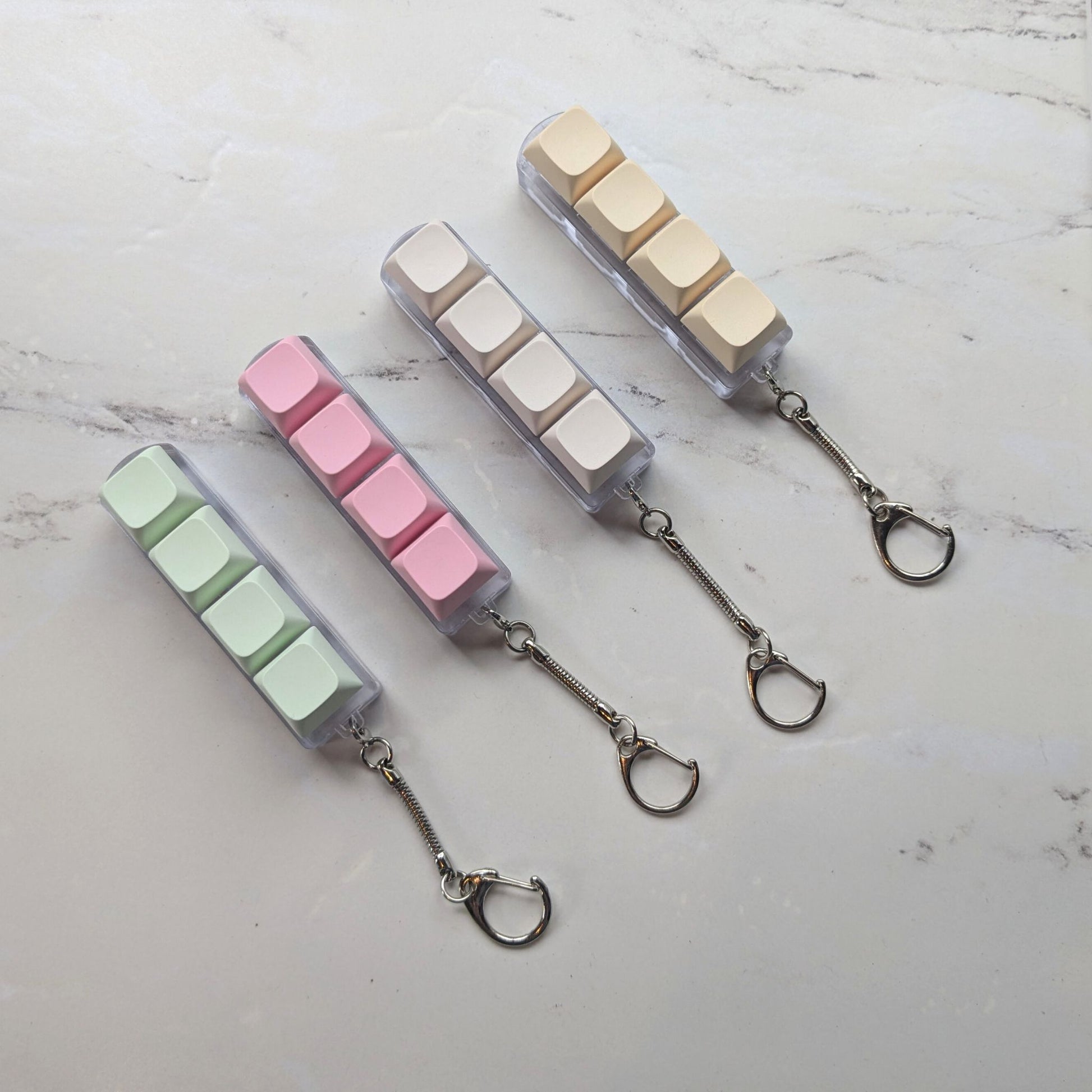 Keyboard fidget clicker keychains in green, pink, cream and beige on a light background