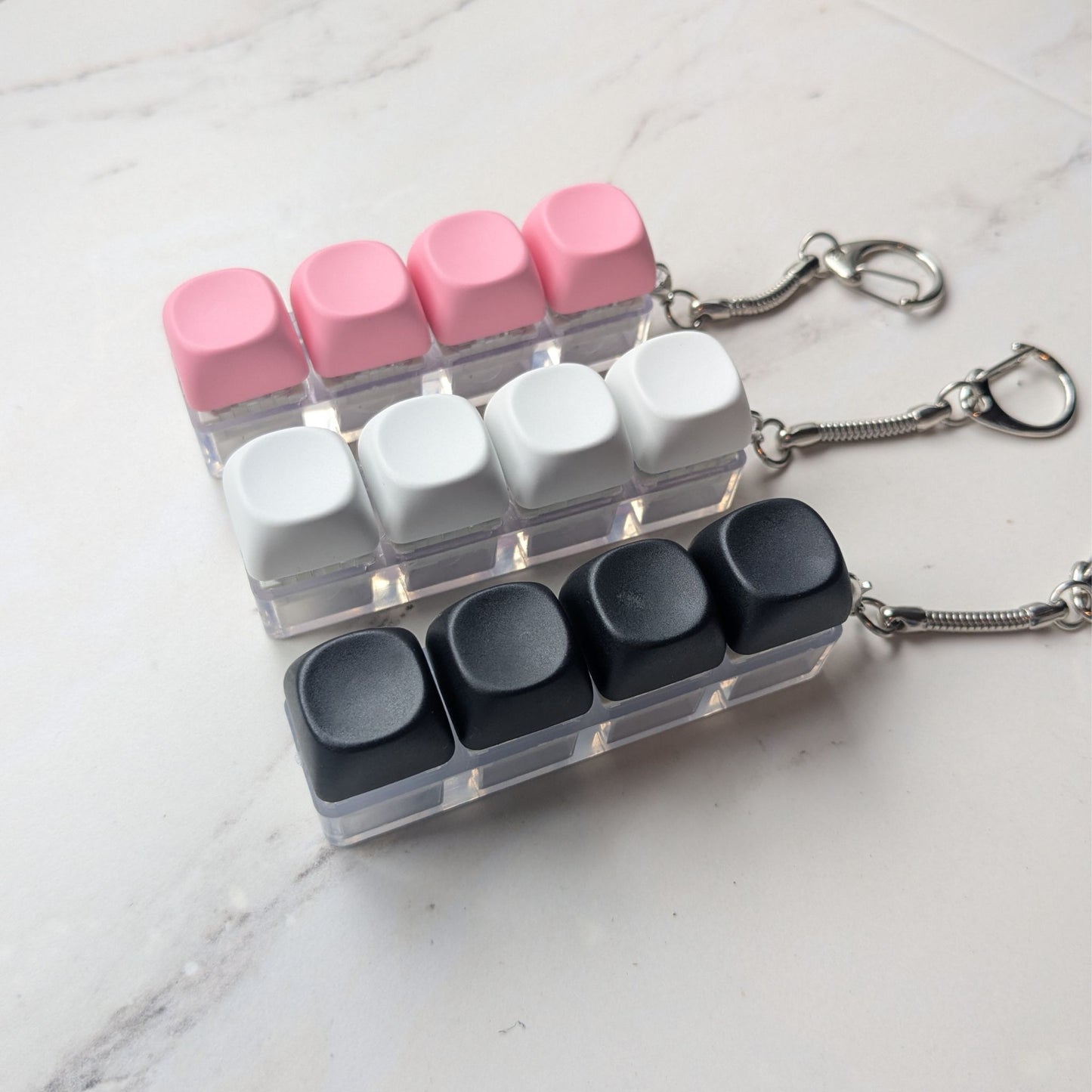 Keyboard fidget clicker keychains in white, pink and black on a light background