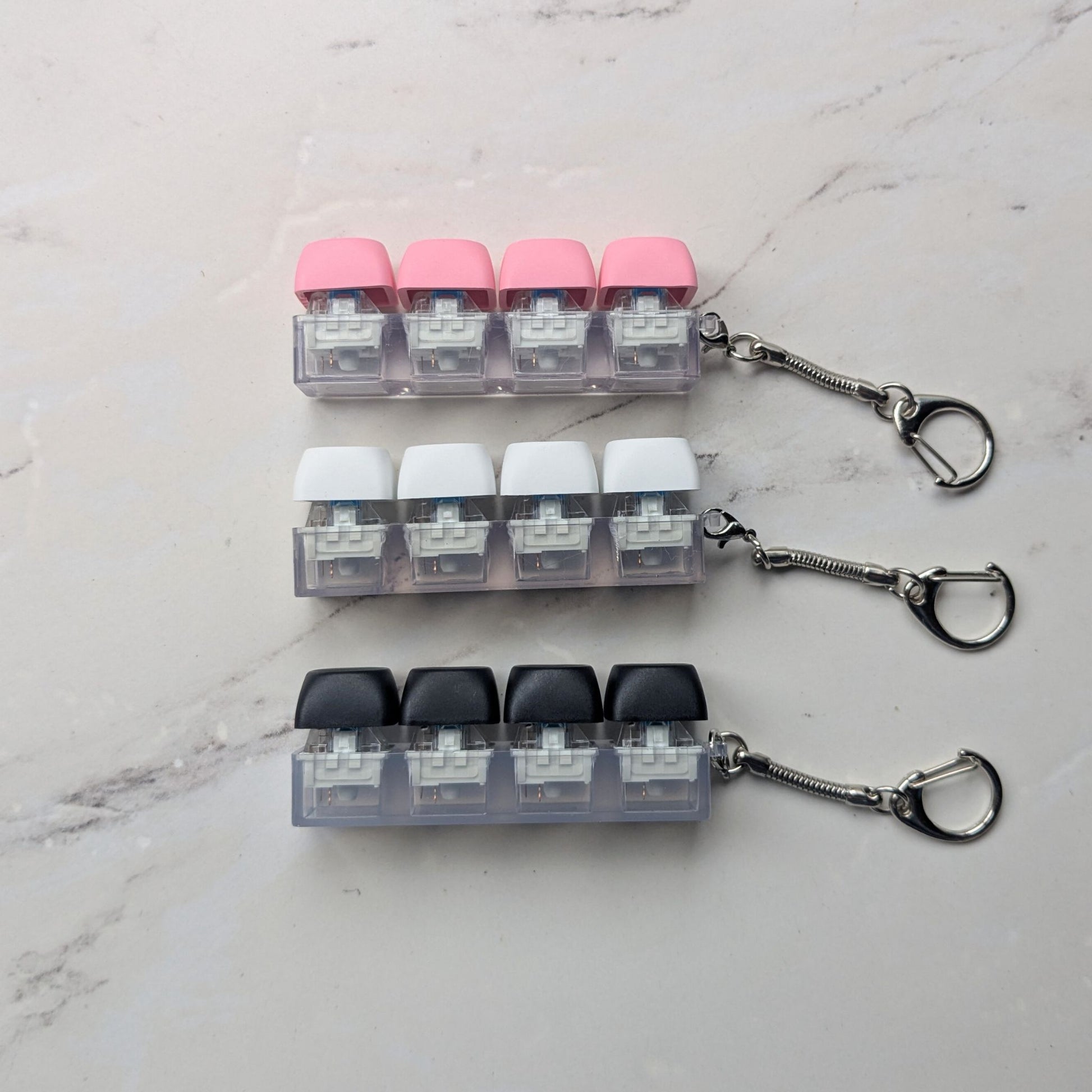 Keycap fidget clicker keychains in green, pink, white and black on a light background
