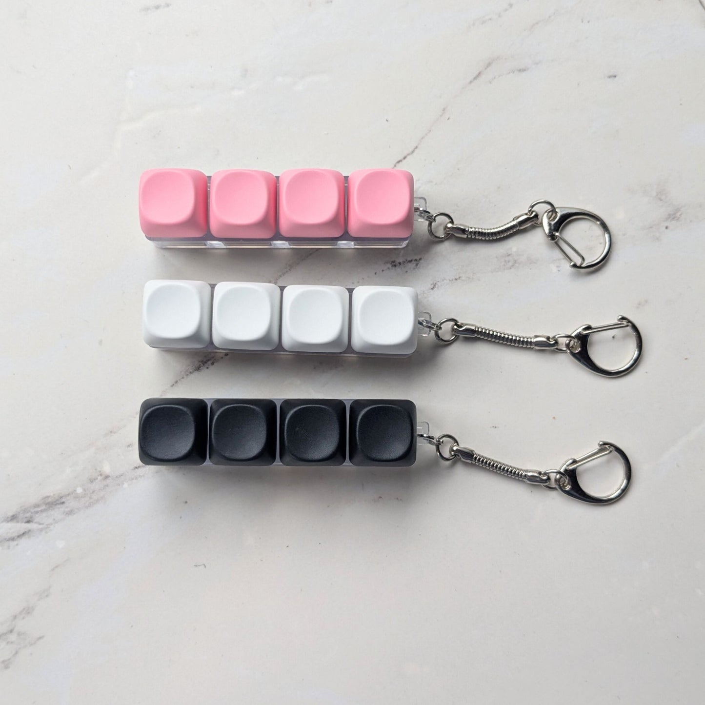 Keycap fidget clicker keychains in pink, white, and black on a light background
