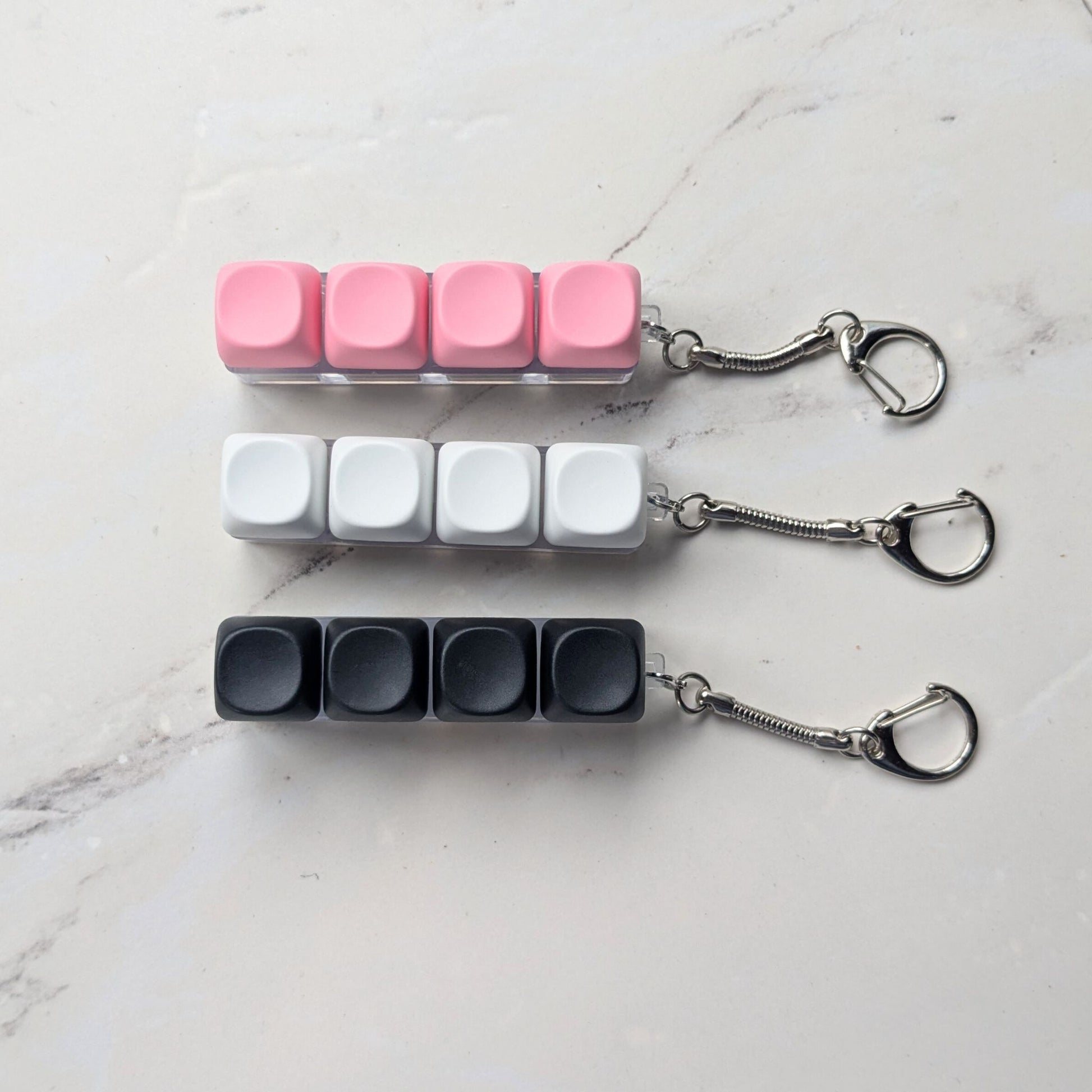 Keycap fidget clicker keychains in pink, white, and black on a light background