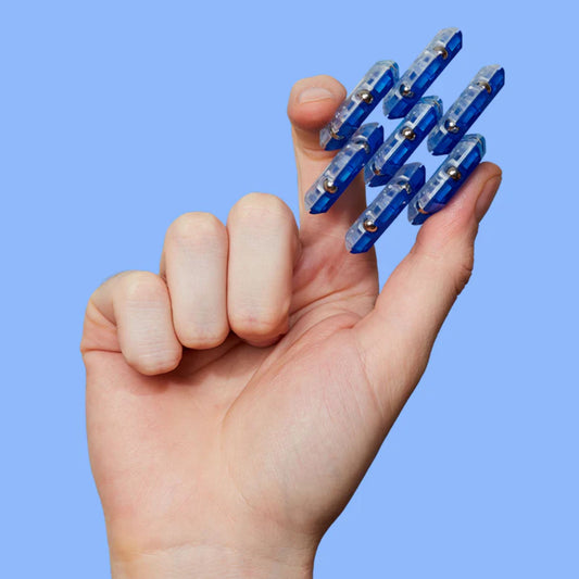 Hand holding a Speks magnetic fidget for adults and teens in cobalt blue against a blue background