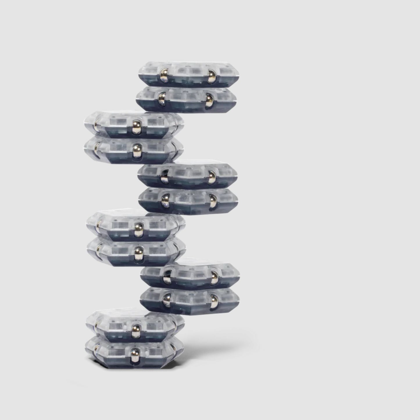Stack of clear and grey Speks Geode magnetic fidget sphere pieces in a tower structure on a light grey background