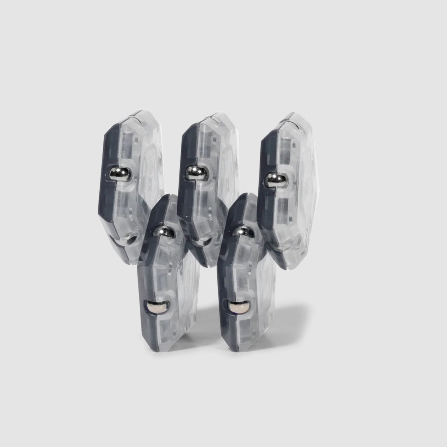 Set of five clear and grey Speks Geode magnetic fidget sphere pieces in a horizontal structure on a light grey background