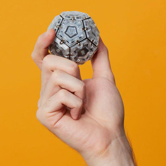 Hand holding a Speks Geode magnetic fidget sphere against an orange background