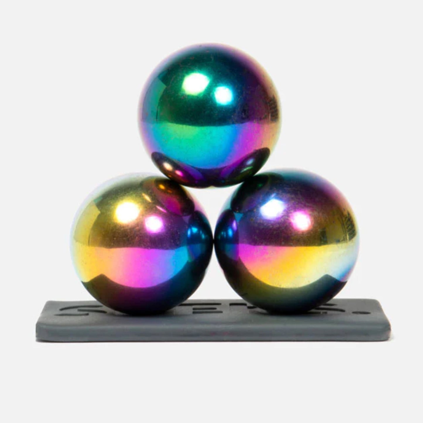 Three Speks Supers oil slick magnet balls stacked on a gray base against a white background