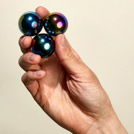 Hand holding three Speks Supers oil slick magnet balls against a beige background