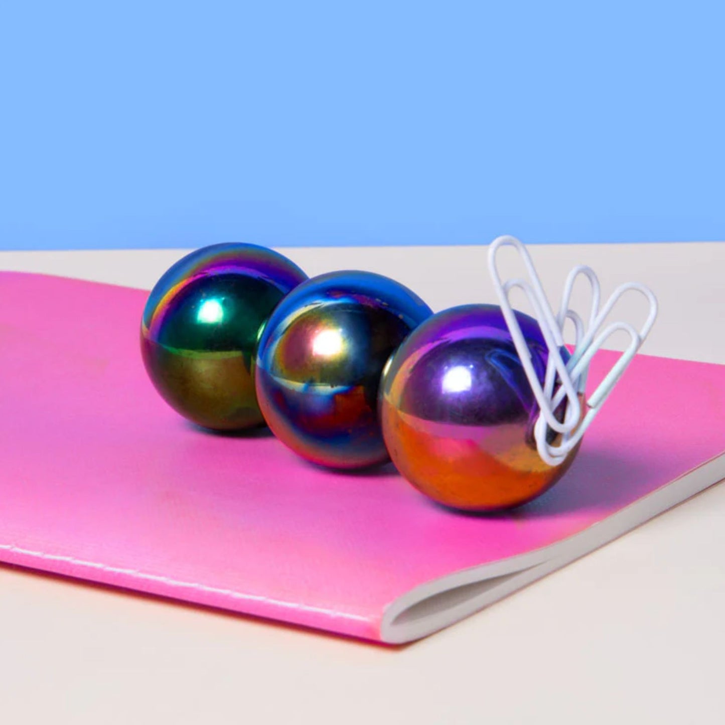 Three Speks Supers oil slick magnet balls on a pink books with white paper clips stuck to them