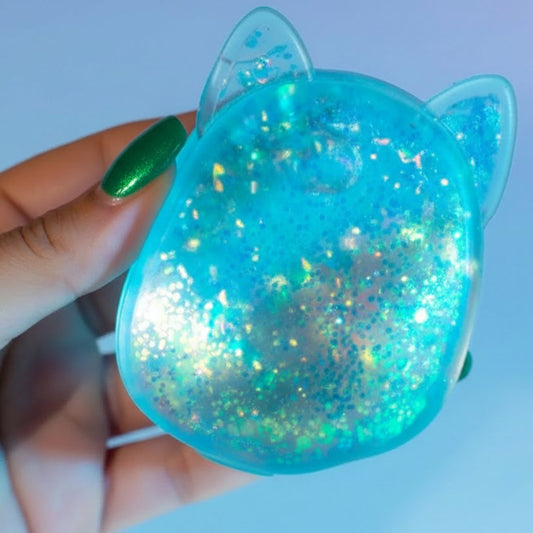 Blue glittery cat-shaped Squishmallow squishy toy held in a hand against a light blue background