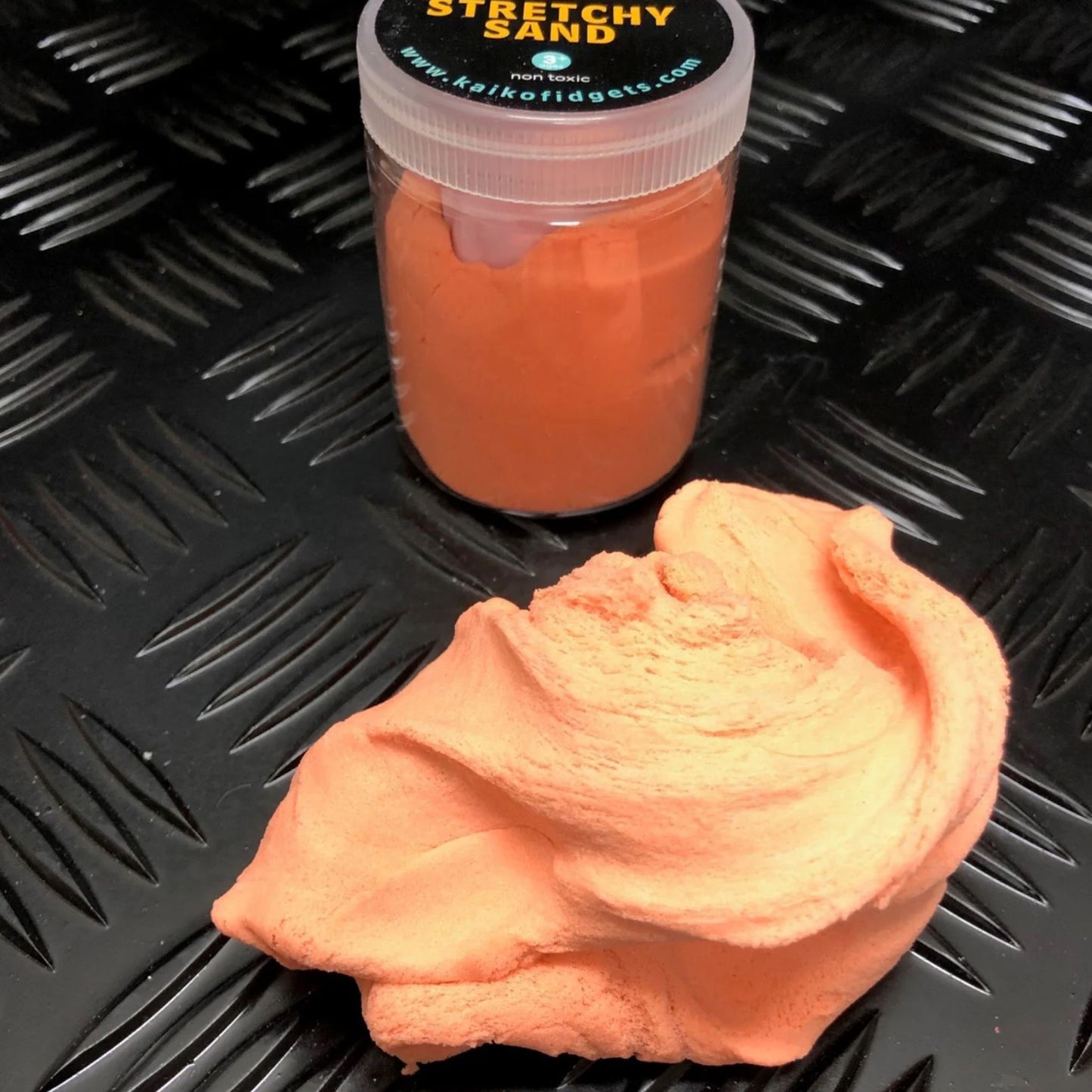 Orange stretchy sand with a container on a textured black surface