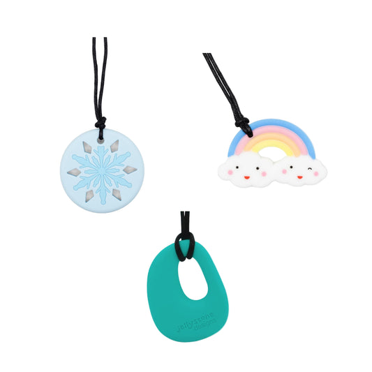 Three colourful chew necklaces with snowflake, rainbow, and cloud pendants on a white background.