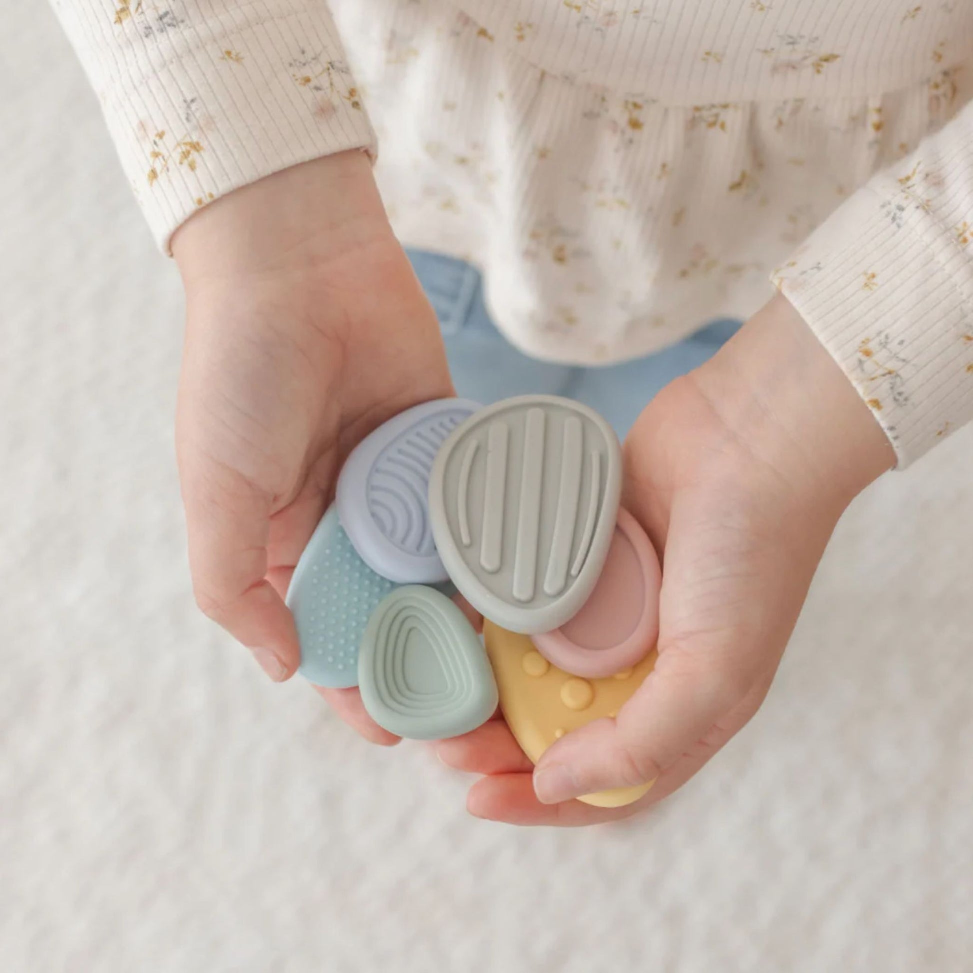 Child's hands holding four small, pastel-coloured silicone worry stones.