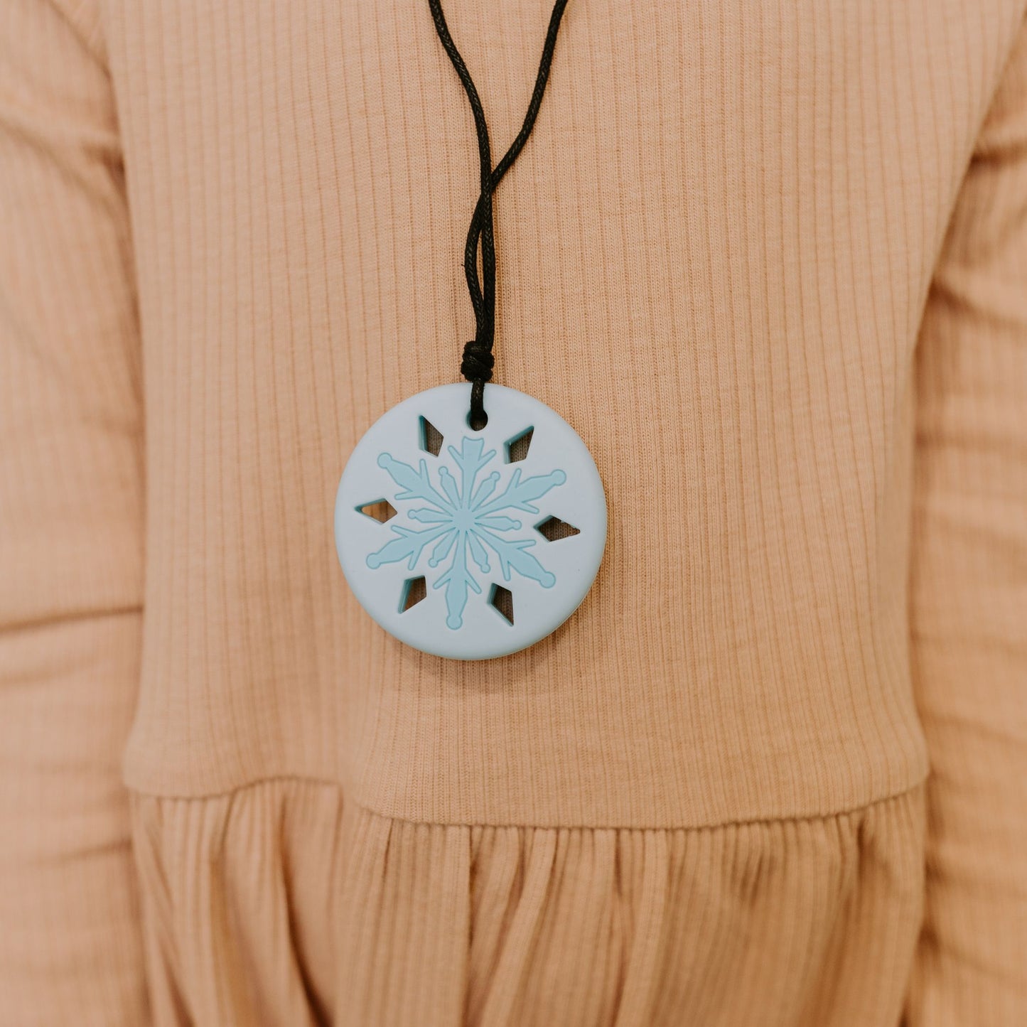 A blue snowflake chewing necklace with on a beige background