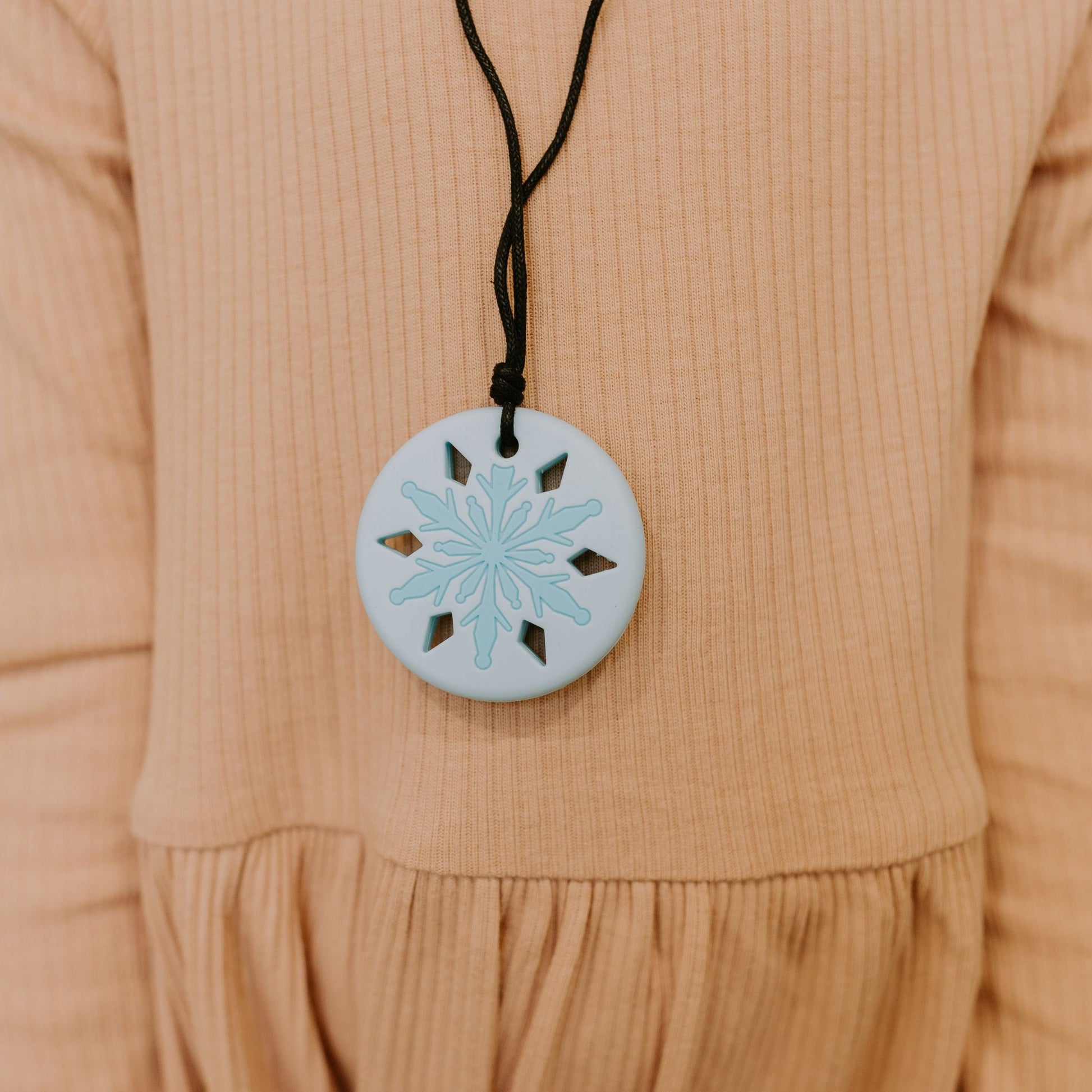 A blue snowflake chewing necklace with on a beige background