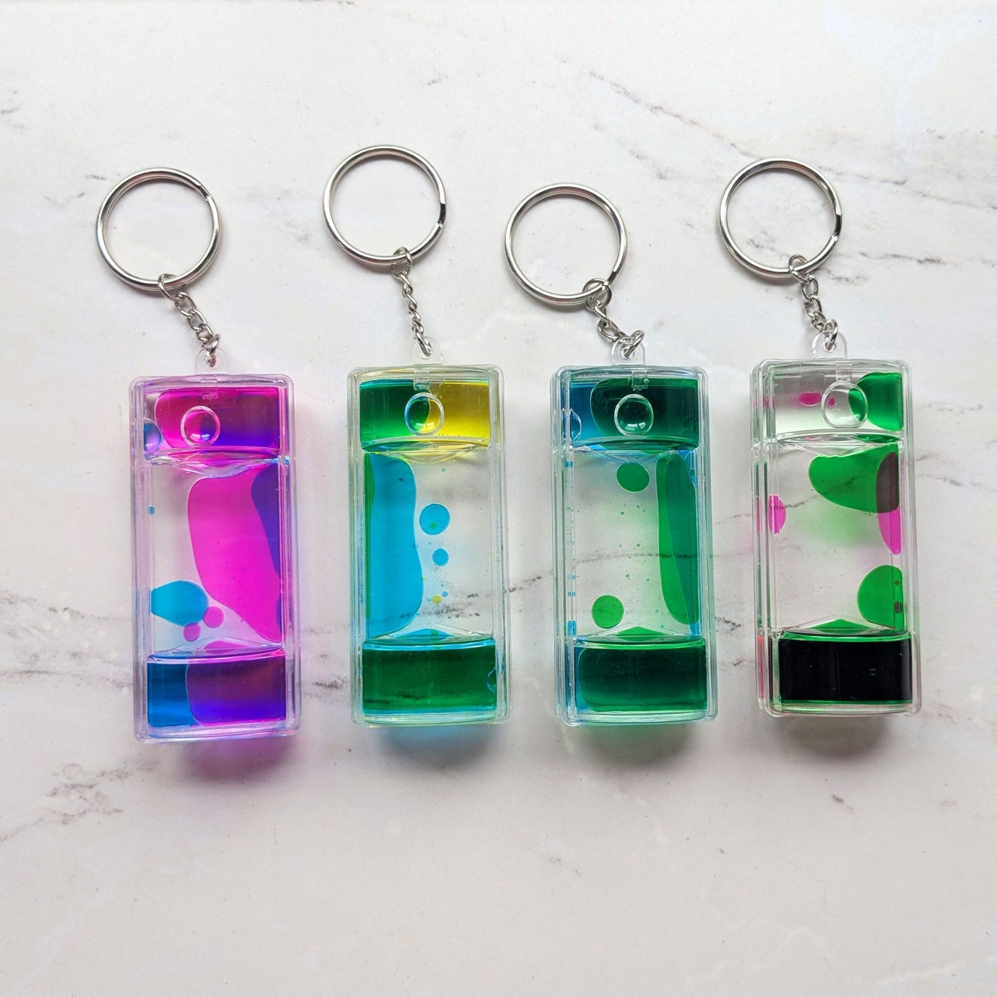 Set of four colourful liquid timer fidget keychains on a marble surface
