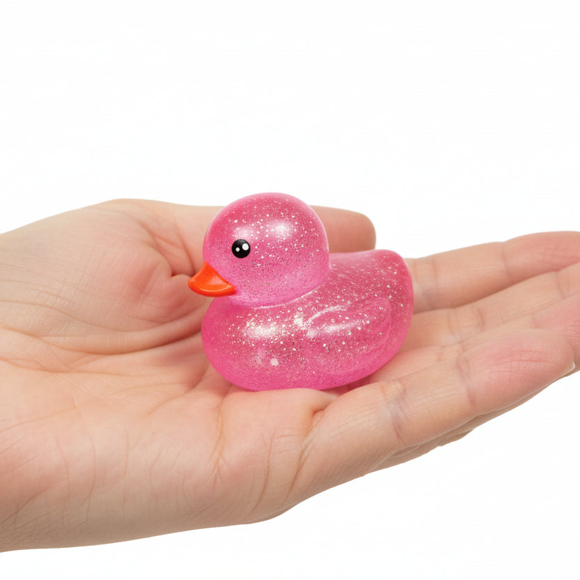 Pink glittery squishy duck held in a hand on a white background
