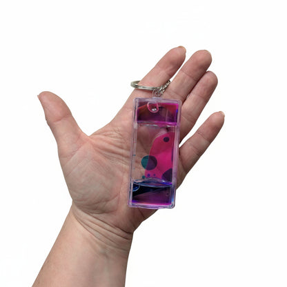 Hand holding a transparent keychain with a colorful design on a light background
