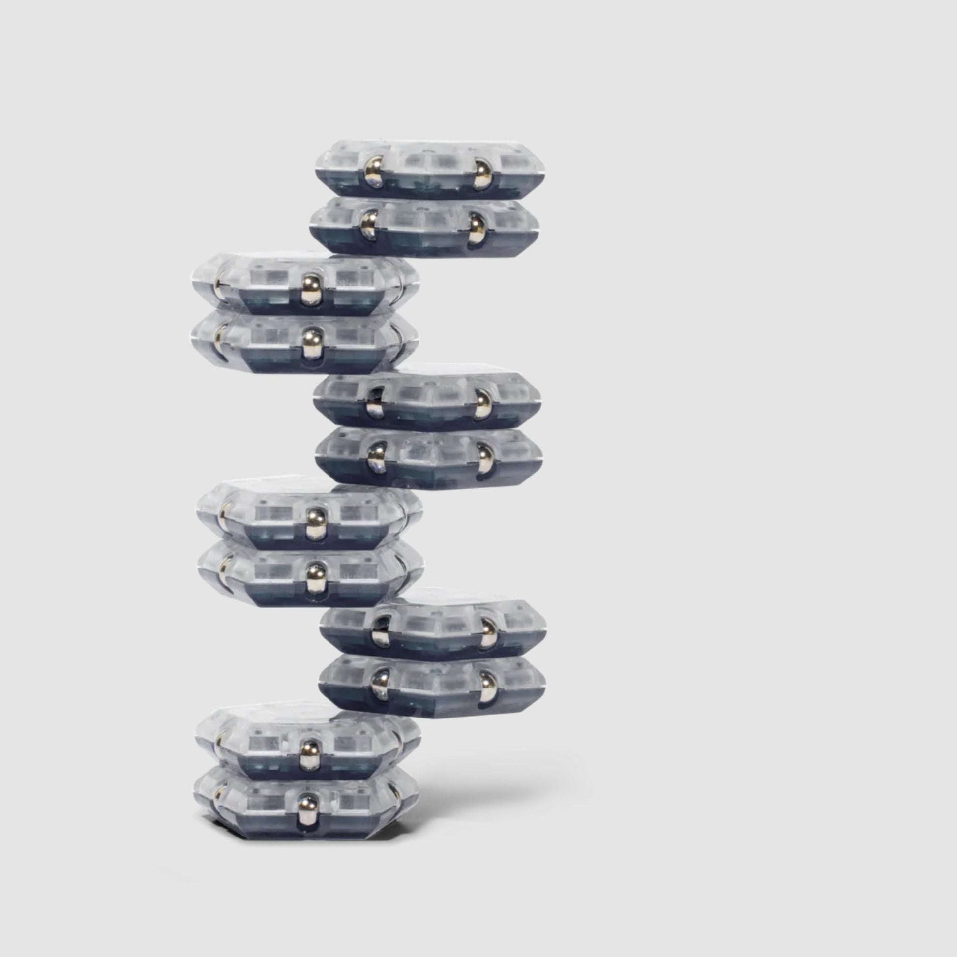 Stack of clear and grey Speks Geode magnetic fidget sphere pieces in a tower structure on a light grey background