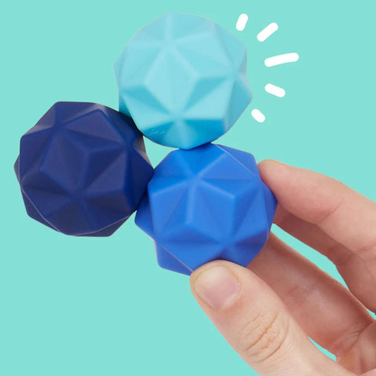 Hand holding three blue geometric Speks Odds silicone magnet balls against a teal background