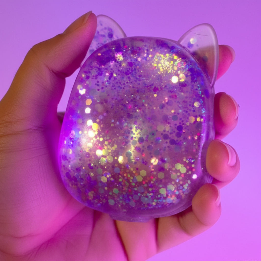 Hand holding a glittery, cat-shaped squishy object against a pink background