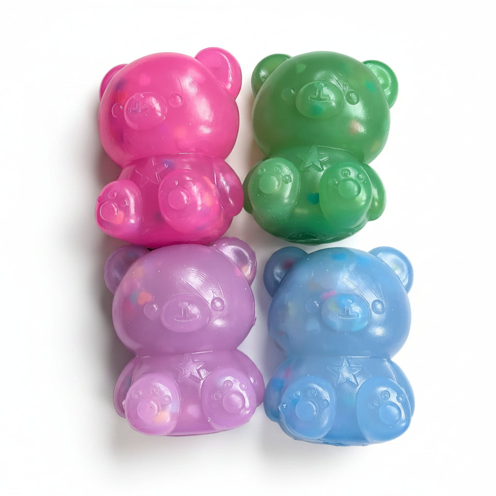 Four translucent teddy bear-shaped squishies in pink, green, purple, and blue, arranged in a 2x2 grid on a light marble surface.